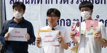 Netiwit Chotiphatphaisal (centre) holding a piece of paper saying "End military conscription" during his protest at the Bang Pu Subdistrict Municipal Office, which was being used as a military conscription centre on 5 April.