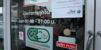 A pharmacy participating in the initiative with an NHSO "quality pharmacy" label at the door.