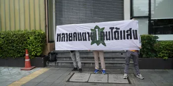 Protesters standing at the university entrance holding a banner saying “Many people died. One person gets attention.”