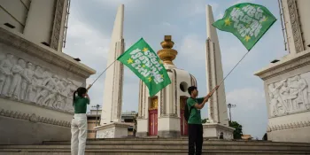 Two people standing near the Democracy Monument ahead of a campaign march for a vote in favour of a new Constitution in the 8 February referendum, holding green flags used as symbols of the campaign. (Photo: Ginger Cat/File photo)