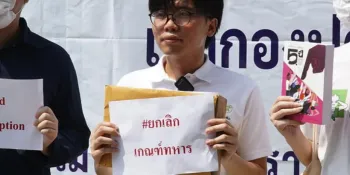 Netiwit Chotiphatphaisal (centre) holding a piece of paper saying "End military conscription" during his protest at the Bang Pu Subdistrict Municipal Office.